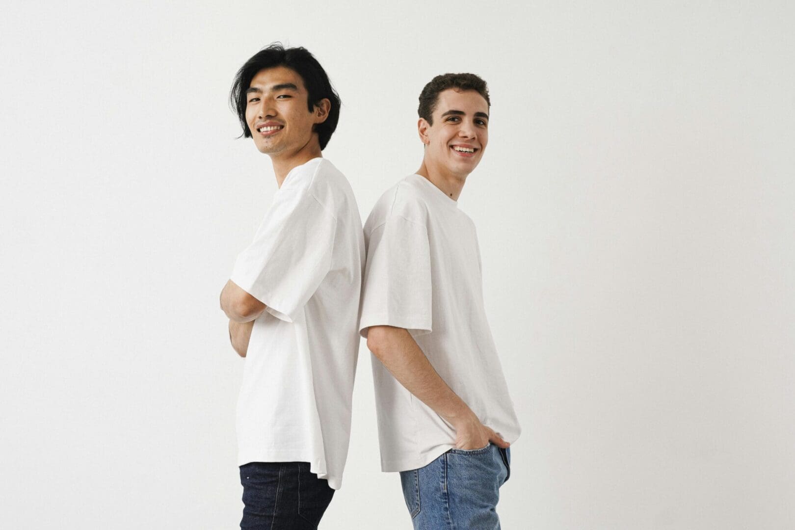 Two men smiling and standing back-to-back, wearing white t-shirts against a plain background.