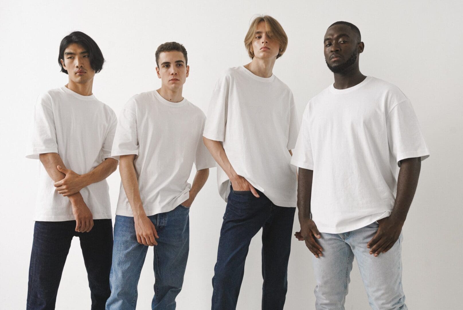 Four men in plain white t-shirts and jeans standing against a white background.